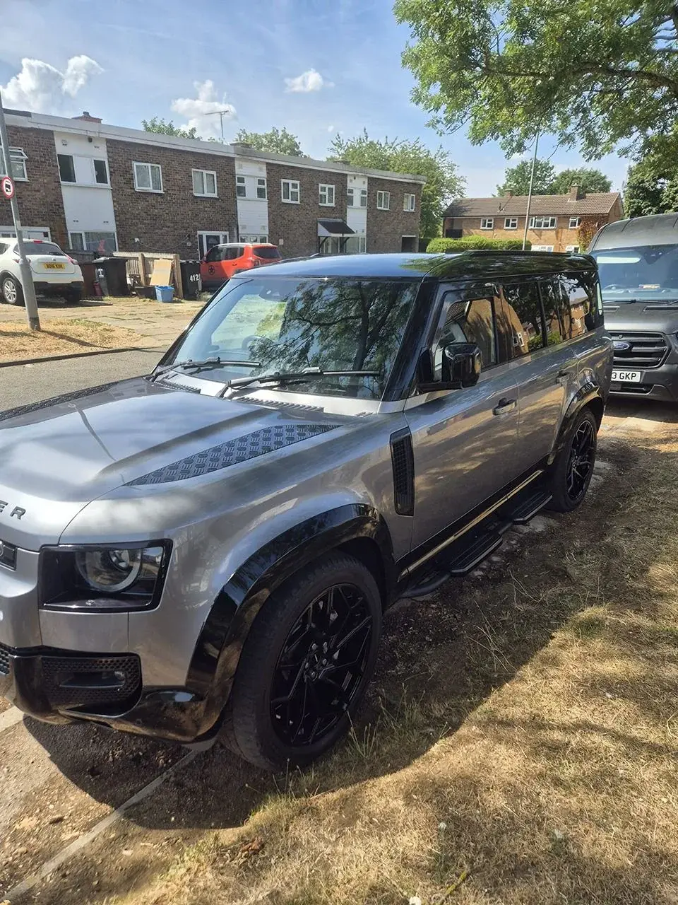 Silver Land Rover Defender with black wheels parked at the kerb, with the VPA van parked on the right