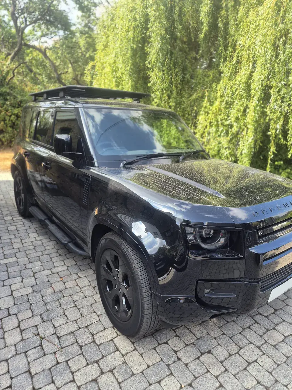 Black Land Rover Defender with a mirror shine under the trees