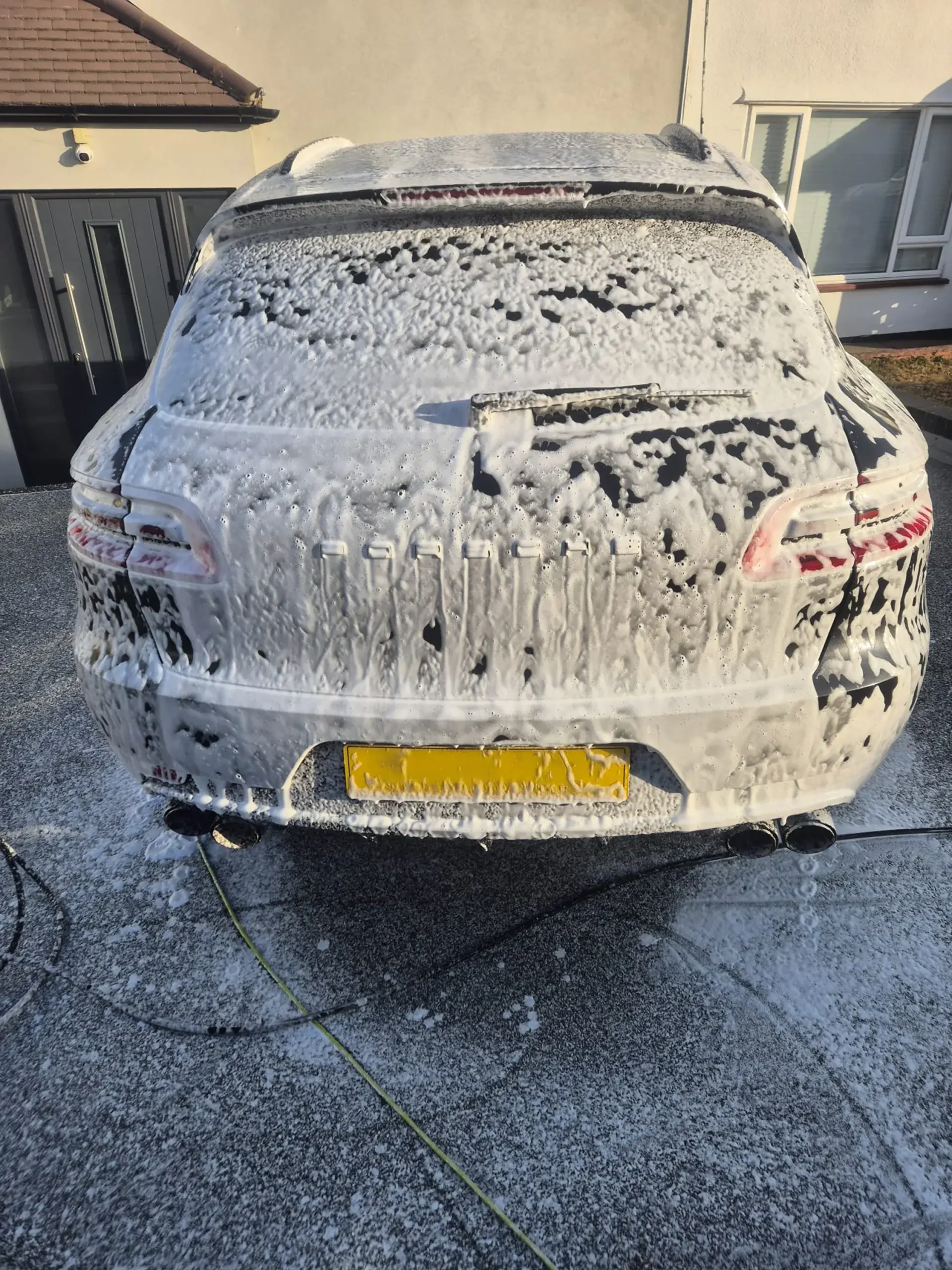 An SUV covered in snow foam during a car wash on a driveway